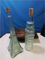 2 tall oil glass bottles one in the shape of the