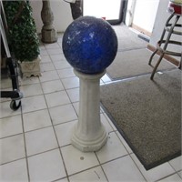 Blue gazing ball on concrete pedestal.