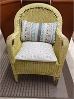 Wicker patio chair in yellow with accent pillows.