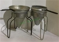 Set of two vintage aluminum strainers on stands.