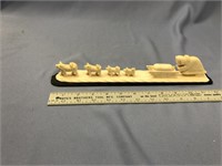 A carved bone dog sled team mounted on a piece of