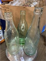 three green soda bottles with embossed origins
