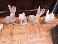 Four concrete yard ornaments of rabbits, all