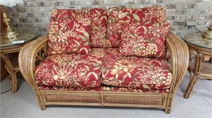 Wicker love seat with red tropical cushions.