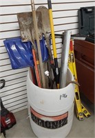 plastic barrel with long handled tools and misc