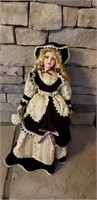 Blonde haired porcelain doll on stand approx 22
