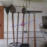 Tools hanging on wall:  rake, fork, shovel,