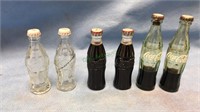 Six miniature Coca-Cola bottles with caps, three