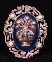 A large oval pin with floral relief, blue stone