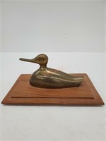 Brass duck on wooden platform.