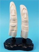 2 Whales teeth carved into 2 figures on a wooden d