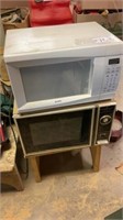 2 microwaves both power on, plus wood stand