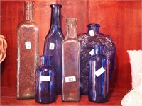 Six bottles, blue and green in color, ranging