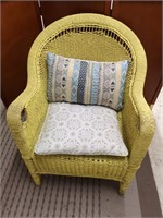 Wicker patio chair in yellow with accent pillows.
