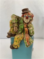 Porcelain clown sits on the edge of a shelf g