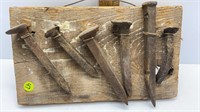 6 VINTAGE RAILROAD SPIKES ON A PIECE OF WOOD