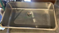 Large stainless steel sink with a drain.