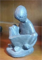 Bronze colored statue of a boy reading a book