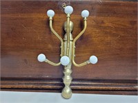 Brass wall mounted coat rack with porcelain nobs.