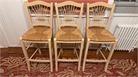 Three blonde wood barstools, with a woven rush