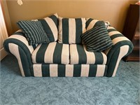 Green and cream striped loveseat with pillows.