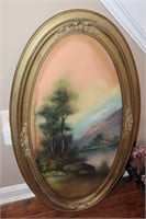 Oval framed picture of a tree, river and m